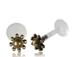The Kaya Movement LUST Flower Labret Stud in Gold features a minimalist tribal design. These 16 gauge gold brass body jewelry lip studs have flower-shaped ends, each adorned with a central round bead surrounded by smaller round beads that mimic petals. The posts are crafted from clear, smooth bio-plastic push back material for added comfort and ease of wear.