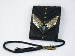 The AMONI Gold Stud Bi-Fold Flip Black Leather Wallet from Kaya Movement boasts gold triangular embellishments forming a wing-like pattern on its flap, centered with a labradorite stone. It includes a braided strap with a metal clasp for attachment. This custom leather wallet is ideal for those seeking sophisticated style against a plain white background.