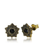 Introducing the OLLY Mandala Stud Earrings by Kaya Movement, featuring intricate gold-colored filigree designs resembling a flower. Each earring has a central black onyx gemstone set within the ornate yellow brass metalwork. The studs have butterfly clasps for fastening, making them perfect ear lobe jewelry.