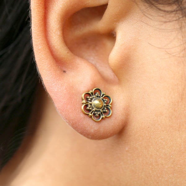 Close-up of an ear adorned with a decorative MIA Flower Stud Earring in Gold from Kaya Movement. This exquisite piece of jewelry features an intricately designed gold floral motif with a central pearl-like bead, crafted from yellow brass and elegantly packaged.