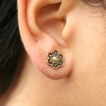 Close-up of an ear adorned with a decorative MIA Flower Stud Earring in Gold from Kaya Movement. This exquisite piece of jewelry features an intricately designed gold floral motif with a central pearl-like bead, crafted from yellow brass and elegantly packaged.