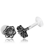 Two BLOSSOM Labret Studs in Silver by Kaya Movement, each with a clear plastic post, lie on a white background. The decorative end of each 16 gauge stud is crafted from 925 silver, intricately designed with small loops and a central raised dot, reminiscent of a delicate tribal beaded flower. Perfect for Stud Earrings Tragus Helix Labret.