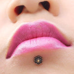 A close-up of a person's lips with vibrant pink lipstick, showcasing a small, decorative BLOSSOM Labret Stud in Silver with a white gem at the center on their lower lip, slightly to the right. The 16-gauge body jewelry by Kaya Movement complements the look perfectly.