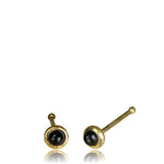 A pair of EDEN Nose Pin Studs by Kaya Movement in gold with small round onyx stones set in the center, reminiscent of minimalist gold earrings. These 20 gauge studs feature cylindrical posts with rounded ends against a plain white background.
