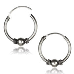 The SPIA Simple Tribal Hoop Earrings in Silver by Kaya Movement are crafted from sterling silver 925 and feature a spherical bead at the center of each hoop, flanked by twisted rope-like designs. These 18 gauge earrings have a smooth, metallic finish and are showcased on a white background with a slight reflection beneath them.