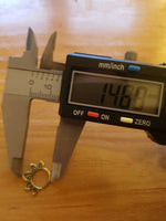 A digital caliper displaying a measurement of 14.80 mm is positioned above the MAWAR Lotus Flower Septum Ring in Silver by Kaya Movement, which is an 18-gauge decorative piece. The ring, resembling tiny hoop earrings often crafted from 925 silver body jewelry, features a petal or leaf-like design around its perimeter. Both items rest on a wooden surface.