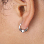 Close-up of a person's ear wearing Kaya Movement's SPIA Simple Tribal Hoop Earrings in Silver (18 gauge). The sterling silver 925 hoop earrings feature two textured areas with a polished bead in the center, adding distinct details to the minimalist design. The skin around the ear appears smooth.