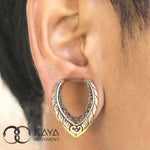 Close-up of an ear adorned with a MYRI Tribal Saddle Tunnel in Gold, sized 12mm to 25mm gauge, featuring intricate ethnic patterns. The tunnel boasts a rich mix of metallic colors and detailed designs with brass accents. The Kaya Movement logo is visible in the bottom left corner of the image.