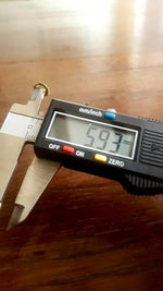 A digital caliper displaying a measurement of 6.93 millimeters is being used to measure the diameter of the IRI Seamless Tragus Ring in Gold | 18 gauge from Kaya Movement. The yellow brass caliper, featuring an on/off button and a zero reset button, displays measurements in millimeters.