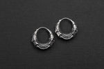 A pair of Silver Futuristic Hoop Earrings by Kaya Movement, showcasing intricate detailing and a layered design, displayed on a plain black background. These unisex earrings, featuring a secure snap latch closure, have a metallic sheen and a unique, SciFi-inspired appearance perfect for tech lovers.