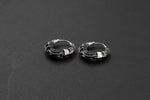 The Silver Futuristic Hoop Earrings by Kaya Movement are showcased against a dark backdrop, highlighting their intricately detailed sterling silver craftsmanship. Each earring features a rough, organic design with interwoven metal strands, creating a distinctive and rugged look. The secure snap latch closure enhances the practicality of these cyberpunk-inspired pieces, making them perfect for tech lovers and everyday wear.