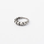 The AARO Cyborg Clicker Hoop Septum Nose Ring in Silver by Kaya Movement, featuring interconnected rectangular segments that resemble linked blocks, lies on a plain white surface. Its rugged and textured design evokes dystopian body jewelry, making it a striking piece for any futuristic fashion enthusiast.