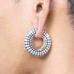 A close-up of an ear adorned with a large, circular SILO Seamless Hoop Ear Weight in silver from Kaya Movement. The earring features intricate black and white patterns, with alternating black and silver sections that make a bold statement.