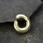 A close-up image of the DAYA Minimalist Hoop Ear Weights in Gold with a clicker by Kaya Movement, featuring a smooth and polished finish. The 2 gauge earring rests on a textured, dark gray stone surface—perfect for those seeking stylish unisex body jewelry.