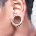Close-up of a person's ear wearing a large, crescent-shaped earring from Kaya Movement. The earring is a Dragon Scale Horseshoe Saddle Tunnel in gold, featuring a textured crisscross pattern resembling reptile skin. The earring size ranges from 12mm to 18mm gauge. The individual's skin and hair are visible in the image.