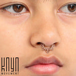 Close-up of a person's face, focusing on the MAWAR Lotus Clicker Septum Ring in Rose Gold (16 gauge) by Kaya Movement, a decorative piercing with a floral design. The brown-eyed individual has a neutral expression. The logo "Kaya Movement" is visible in the bottom left corner.