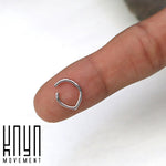A small, silver TIKA Teardrop Clicker Ring in 316 Surgical Steel, with a 16 gauge design, balances delicately on a fingertip. The background is white and the words "Kaya Movement" are printed in black in the lower-left corner, showcasing a minimalist aesthetic.
