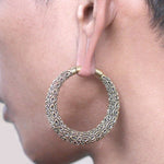 Close-up image of a person's ear wearing the PAWA Tribal Thick Hoop Ear Weights in Gold with Clicker (6 gauge) by Kaya Movement. The ornate brass jewelry showcases a detailed, textured design covering its surface. The neutral background ensures the focus remains on these striking earrings.