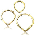 Three TIKA Minimalist Teardrop Seamless Rings in Gold by Kaya Movement are arranged in a triangular pattern. These 16-gauge gold rings have a teardrop shape with a subtle clasp on one side. The reflective surface below creates a faint mirrored effect of the minimalist teardrop rings.