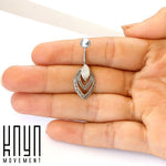 A person's hand is holding the IBASA Marquise Belly Piercing Ring in Silver & Mother of Pearl, a 14-gauge belly button ring with intricate designs and a white Natural Mother of Pearl stone in the center. The logo "Kaya Movement" is displayed in the lower left corner of the image. The background is white.