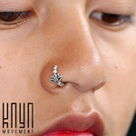 Close-up of a person's nose adorned with Kaya Movement's Lotus Flower Seamless Nose Ring in Silver (20 gauge), showcasing its tribal ethnic Lotus design. The smooth skin reflects the highlighting light, capturing a shiny surface on the nose ring. The logo "Kaya Movement" is in the bottom left corner.