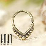 A decorative gold LILY Seamless Teardrop Septum Ring in Gold | 18 gauge with intricate beadwork on a blurred neutral background. The bottom of the ring features a series of small gold beads in varying sizes, creating a beaded tribal design. The logo "Kaya Movement" is displayed in the lower left corner in black text.