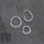 Three pieces of silver jewelry from Kaya Movement, featuring a beaded tribal ethnic design, are arranged on a textured dark surface. They vary in size, with one being a larger, complete circle and the other two smaller semi-open rings from the ITA Seamless Ring in Silver collection (16 gauge). "Kaya Movement" is inscribed in the bottom left corner.