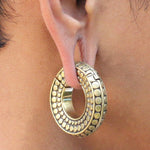 Close-up of a person's ear adorned with Kaya Movement's SILO Seamless Hoop Ear Weights in Gold with Clicker (1/2 gauge). The circular earring features a ridged pattern and small raised dots. The ear appears to be stretched with expander ear hangers to accommodate the striking jewelry piece.