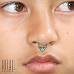 A close-up of a person's face highlights their nose adorned with the ANI Seamless Septum Ring in Gold & Turquoise by Kaya Movement. Their smooth, slightly tan skin is complemented by the 16-gauge jewelry. In the bottom left corner, the text "Kaya Movement" is visible, indicating an appreciation for gold brass body jewelry.