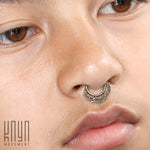 Close-up of a person wearing the MANDA Mandala Septum Ring in Gold by Kaya Movement, showcasing its intricate, bronze-colored details reminiscent of tribal ethnic mandalas. The piercing is prominently featured in the image, against the backdrop of the person’s smooth skin and full lips. The bottom left corner features the text "Kaya Movement.
