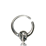 The SKULL Gothic Septum Ring in Silver by Kaya Movement boasts a detailed skull design at its center, with the top of the ring partially open. Crafted from 18 gauge 925 silver body jewelry, the skull exhibits intricate detailing in its features, creating a bold and edgy look. The ring is showcased against a white background.