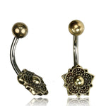 The Lotus Mandala Belly Piercing Rings in Gold, by Kaya Movement, are beautifully showcased. Each 14 gauge navel piece features a small golden ball on one end and a larger end adorned with an intricately designed floral pattern highlighted by a central golden ball. Crafted from 316L surgical steel, these belly button rings come elegantly packaged for gifting.