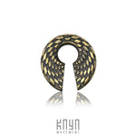 An intricate, metallic pendant named "DAMIER Checkered Hoop Keyhole Ear Weights in Gold | 0 gauge" from Kaya Movement features a geometric, checkered pattern in gold and black. It includes a narrow keyhole opening at the bottom leading to a circular hole in the center. Below the pendant, the text "KNYN MOVEMENT" is displayed.