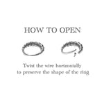 Diagram showing how to open the AARO Cyborg Seamless Hoop Septum Nose Ring in Gold by Kaya Movement. The image displays two rings: one is closed on the left, and the other is partially opened on the right with an arrow pointing to the open end. The text instructions read, "Twist the wire horizontally to preserve the shape of your 18 gauge gold brass hoop ring.