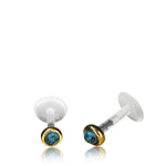 The KEA Labret Stud in Gold & Turquoise by Kaya Movement features small, round natural turquoise stones set in gold-colored rims. The 16 gauge brass jewelry has clear posts with flat, round backings. Subtle black veining on the turquoise stones adds texture and detail to the design.