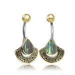 Introducing the IKOSA Fan Belly Piercing Ring from Kaya Movement in Gold & Abalone Shell. This 14 gauge piece is elegantly crafted in surgical steel, featuring a golden curved barbell design with a round golden ball at the top and an intricate shield-shaped pendant at the bottom. The pendant boasts a decorative pattern and an iridescent, teardrop-shaped abalone shell centerpiece.