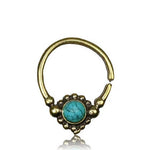 The SYN Seamless Septum Ring in Gold & Turquoise from Kaya Movement features a gold brass body and is adorned with a circular blue turquoise gemstone at the center, surrounded by small beaded details. This 18-gauge, versatile nose ring has an open design with smooth, rounded ends.