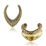 Two gold-colored, intricately designed MYRI Tribal Saddle Tunnels by Kaya Movement are shown side-by-side. Each tunnel has a V-shape with ornate ethnic patterns, giving them a vintage and antique look. The left tunnel's detailed front and the right tunnel's inner curve are visible. These pieces come in gauges ranging from 12mm to 25mm.
