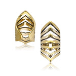 Two pieces of jewelry are displayed, each featuring geometric chevron designs with multiple overlapping V-shaped patterns. One piece is shown at a slight angle, revealing its open back, while the other is presented front-facing. These simple minimalist accessories have a polished finish reminiscent of an adjustable ear cuff. They are the LORA Chevron Cage Ear Cuff in Gold from Kaya Movement.