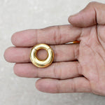 A person's hand holds a smooth, shiny, circular piece from Kaya Movement called the Minimalist Steel Hoop Ear Weights in Gold with Magnet Closure (2 gauge). The background is a neutral, light-colored surface.