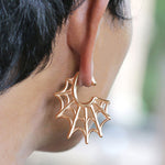 A close-up of an ear adorned with Kaya Movement's Spider Web Gothic Steel Ear Hangers in Rose Gold, sized at 2 gauge. The hangers, echoing the intricate details of tribal design ear weights, possess a unique and stylish flair. The background is blurred, directing attention to the captivating hanger.