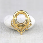 The Sacred Lotus Flower Ear Weights in Gold with Magnet Closure, crafted by Kaya Movement, are showcased resting on a smooth, white pebble against a soft, light-gray background. The intricate and detailed designs of these 2 gauge ear weights highlight their exquisite craftsmanship and elegant design, reminiscent of tribal ear weights.