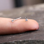 Close-up of a finger with the Kaya Movement Tiny Diamond Silver Nose Pin Stud 20g - Zircon Crystal Gemstone - resting on top. The stud, crafted from Surgical Steel 316L, features a small round-cut zircon crystal. The background is blurry, highlighting the finger and the delicate nose stud with clarity.