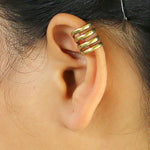 Close-up of a person's ear featuring the KIRA Small Cage Ear Cuff in Gold by Kaya Movement, worn on the upper part of the ear. The minimalist design boasts a smooth finish and hugs the ear without needing a piercing. With an adjustable size for a perfect fit, the person's hair is partially visible.