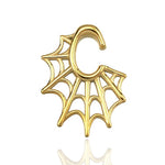 The Spider Web Gothic Steel Ear Hangers in Gold, designed by Kaya Movement, feature an elaborate spider web pattern intertwined with a letter "C" shape at the bottom. This intricate design lends a delicate and ornate appearance to the 2 gauge ear hangers, beautifully showcased against a white background with a slight reflection underneath.