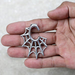 A hand holding a silver keychain shaped like a spider web, reminiscent of the intricate design of the Spider Web Gothic Steel Ear Hangers in Silver | 2 gauge by Kaya Movement. The keychain features a hook at the top for attaching to keys or a bag. The background is a light, neutral color.
