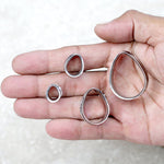 A person's hand holding four silver teardrop-shaped plugs of varying sizes, likely made from stainless steel, designed as ear gauges or flesh tunnels. The hand is open, palm up, with the Teardrop Silver Plugs by Kaya Movement resting on the palm and fingers against a light background.