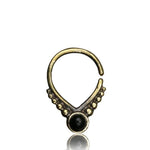 A Unique Gold Triangle Septum Ring with Onyx from Kaya Movement, featuring an 18g design adorned with small dot embellishments on either side and a round black centerpiece at the bottom. The ring has a simple closure at the top, creating a closed loop with a slight gap.