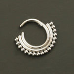 The Nose Piercing Surgical steel Septum Clicker 16g - 8mm Cute Silver Hinged Septum Ring from Kaya Movement boasts a bohemian circular design. This surgical steel piece features a series of small silver beads along the outer edge and a smooth, curved bar at the top, forming a half-moon shape. Set against a plain dark background, it pairs perfectly with any septum nose piercing.