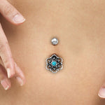 Close-up of a person's belly button adorned with elegant body jewelry. The decorative navel piercing boasts a Lotus flower design, featuring a turquoise gem at its heart and silver accents around it. The person's fingers rest gently on either side of this stunning Kaya Movement Silver 925 Turquoise Belly Ring.
